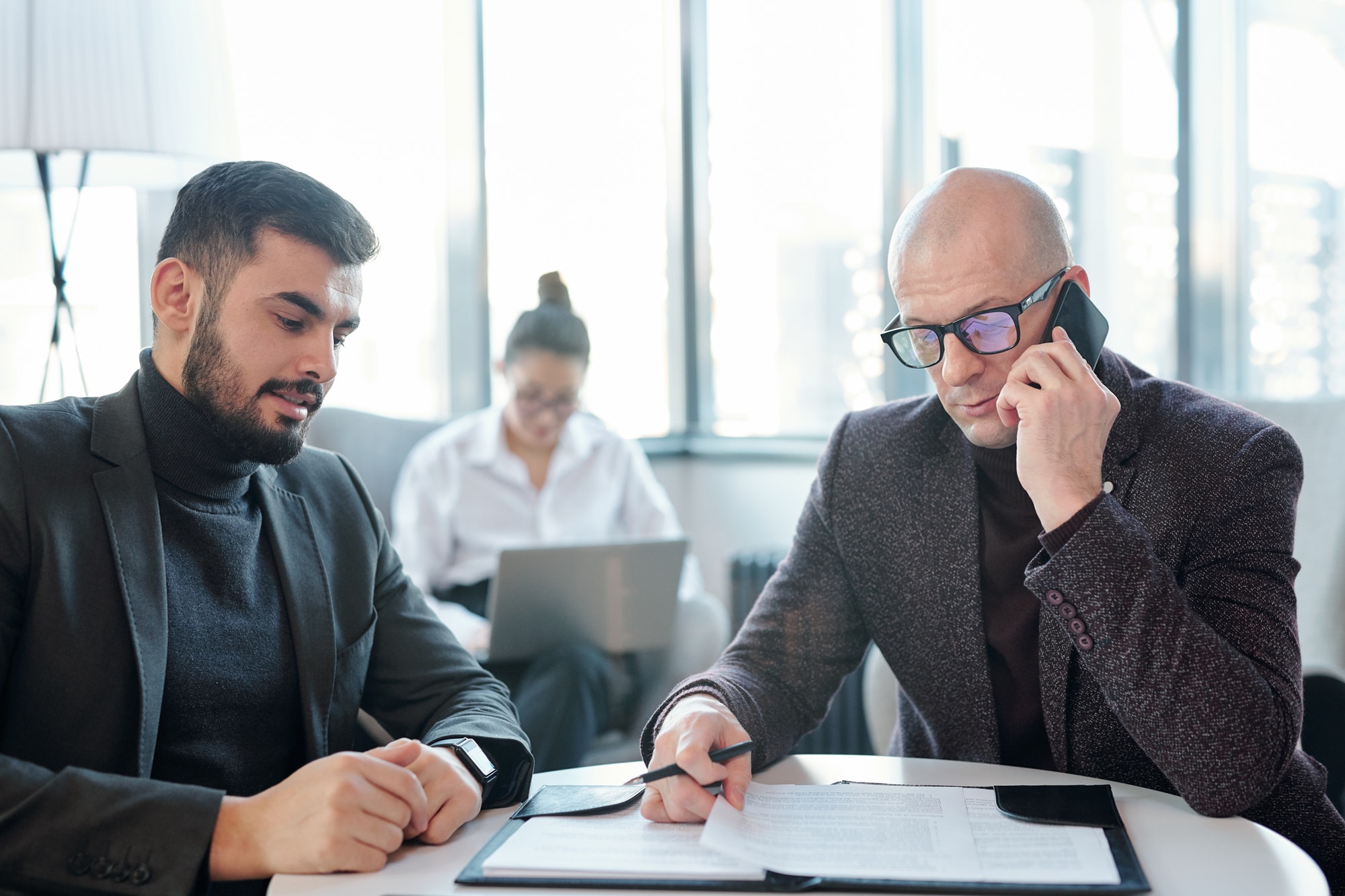 Busy broker in formalwear looking through papers and consulting client by phone
